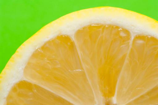 Lemon slice macro showing the succulent tangy acidic pulp within the segments surrounded by a white pith and yellow rind, over green