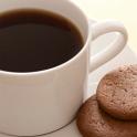 White ceramic cup of freshly brewed full roast black coffee or espresso served with two biscuits on the saucer, high angle close up view