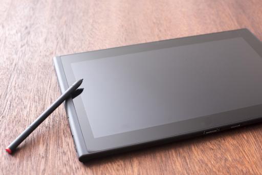 Blank digital tablet with a stylus resting on the side lying on a wooden desk in an oblique angle view