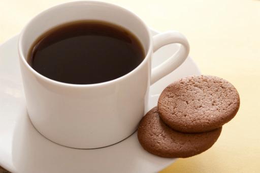 White ceramic cup of freshly brewed full roast black coffee or espresso served with two biscuits on the saucer, high angle close up view