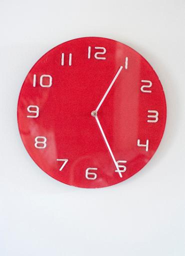 Modern simple circular red clock with Arabic numerals mounted on a white wall with copyspace