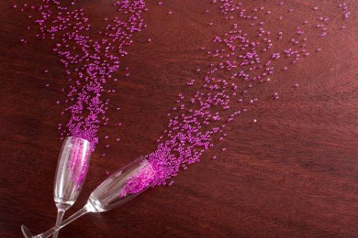 Champagne flutes with pink sequin glitter spilling from them onto a textured wooden surface with copy space for a special message or greeting